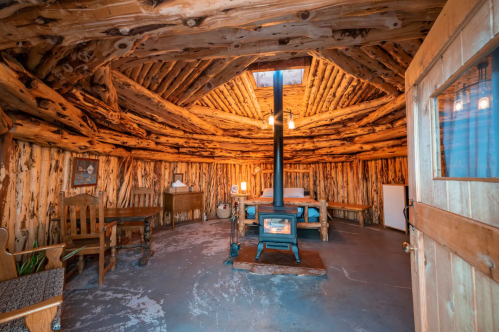 Cozy interior of a rustic cabin with wooden walls, a central stove, and simple furniture. Warm and inviting atmosphere.